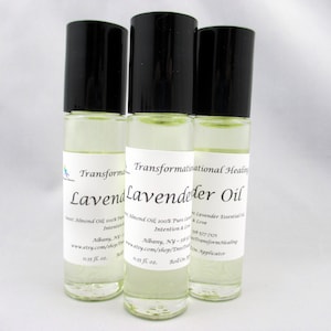 May include: Three clear glass roll-on bottles with black caps, labeled "Lavender Oil." The labels include text about the product and the brand "Transformational Healing." Each bottle contains a light-colored liquid, likely essential oil.