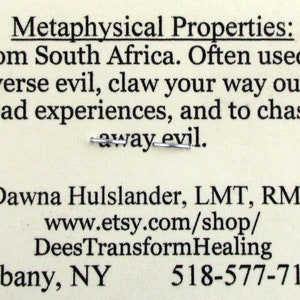 May include: A white card with black text describing the metaphysical properties of a product from South Africa. The text reads: "Metaphysical Properties: From South Africa. Often used to reverse evil, claw your way out of bad experiences, and to chase away evil."