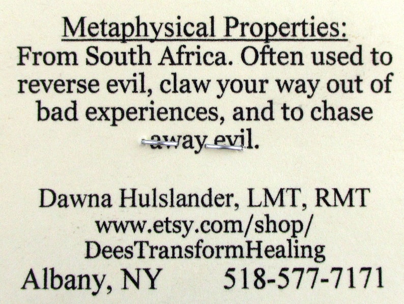 May include: A white card with black text describing the metaphysical properties of a product from South Africa. The text reads: "Metaphysical Properties: From South Africa. Often used to reverse evil, claw your way out of bad experiences, and to chase away evil."
