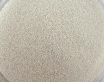 May include: A close-up view of a container filled with fine, white sand. The sand is smooth and uniform in texture, creating a uniform, light beige appearance.