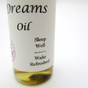 Op de afbeelding: Een klein, doorzichtig glazen flesje met een wit etiket waarop "Dreams Oil" en "Sleep Well Wake Refreshed" staat.