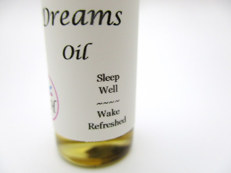 Op de afbeelding: Een klein, doorzichtig glazen flesje met een wit etiket waarop "Dreams Oil" en "Sleep Well Wake Refreshed" staat.