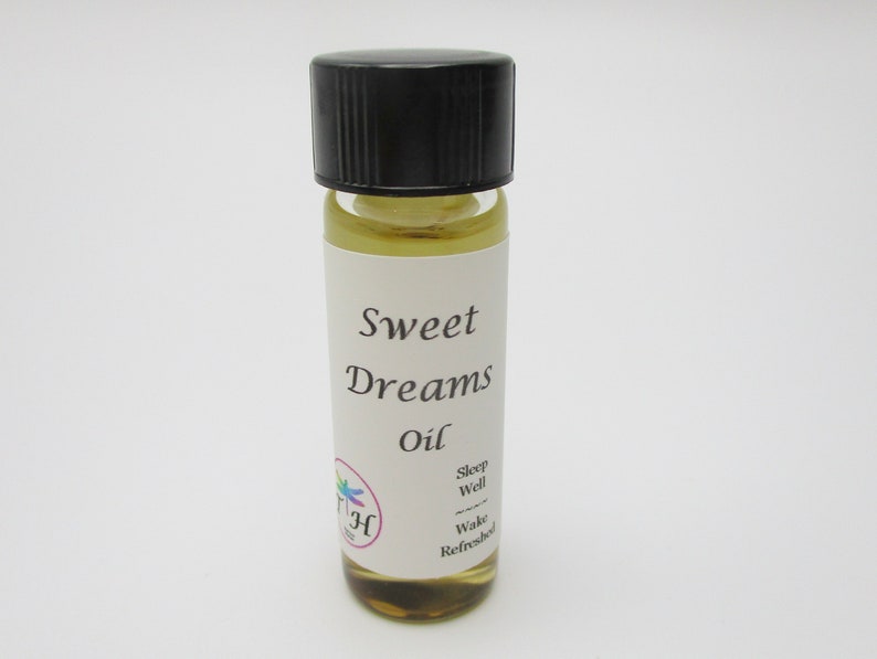 Op de afbeelding: Een klein glazen flesje met een zwarte dop gevuld met een lichtgele vloeistof. Het etiket vermeldt "Sweet Dreams Oil" en heeft een klein libellenlogo. De tekst op het etiket luidt ook "Sleep Well, Wake Refreshed".