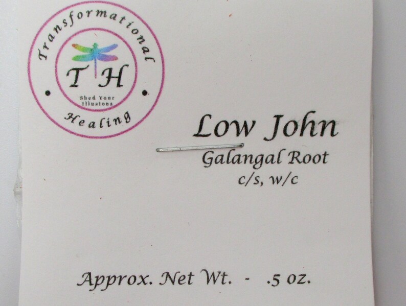 May include: A white label with black text that reads "Low John Galangal Root c/s, w/c Approx. Net Wt. - .5 oz.". A small, round, pink sticker with a dragonfly and the text "Transformational TH Shed Your Illusions Healing" is in the upper left corner.