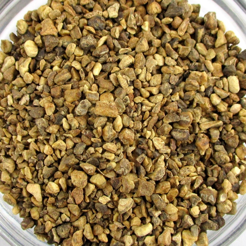 May include: Close-up of a bowl filled with small, irregularly shaped pieces of dried ginger root. The ginger pieces are a light brown color with some darker brown spots.
