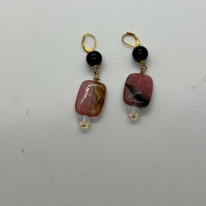 May include: A pair of dangle earrings featuring pink and brown patterned stones, black beads, and gold accents.