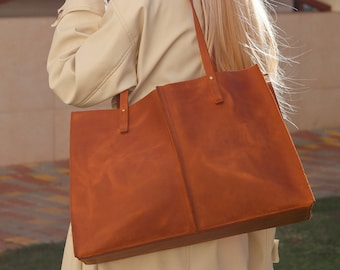 May include: A woman wearing a beige trench coat and sunglasses carries a large brown leather tote bag. She is holding a to-go coffee cup in her right hand.