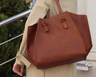 May include: A brown leather tote bag with knotted handles. The bag is worn by a person wearing a beige trench coat and sunglasses.