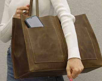 May include: A brown leather tote bag with a phone in the front pocket. The bag has a top handle and a zip closure.