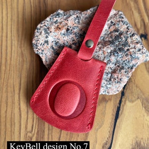 May include: Red leather key fob with a stitched oval design. KeyBell design No. 7.