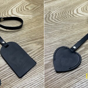 May include: Two black leather keychains with a strap and a tag. The tag on the left is rectangular and the tag on the right is heart-shaped. Both tags have a silver rivet. The keychain on the left has the text "KeyBell Design No.4" and the keychain on the right has the text "KeyBell Design No.3".