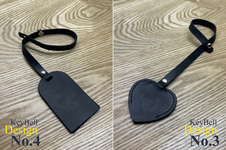 May include: Two black leather keychains with a strap and a tag. The tag on the left is rectangular and the tag on the right is heart-shaped. Both tags have a silver rivet. The keychain on the left has the text "KeyBell Design No.4" and the keychain on the right has the text "KeyBell Design No.3".