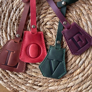 May include: Four leather keychains with the letters L, O, V, and E embossed on them. The keychains are in different colors: brown, red, green, and purple.