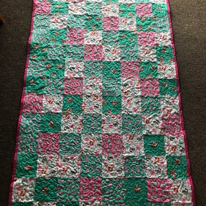 May include: A patchwork quilt with a checkered pattern in pink, white, and teal. The quilt is quilted with a swirl pattern.