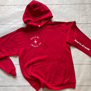 May include: Red hooded sweatshirt with white text that reads "Heir to the Starborn Fire" on the front and "Through love, all is possible" on the sleeve.
