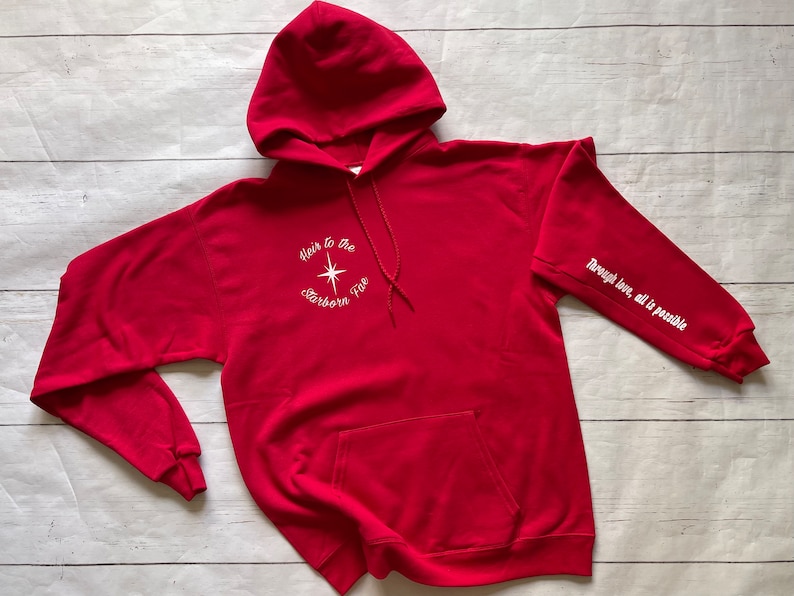 May include: Red hooded sweatshirt with white text that reads "Heir to the Starborn Fire" on the front and "Through love, all is possible" on the sleeve.