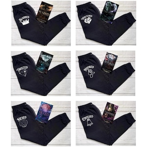 May include: Six pairs of black sweatpants with a white graphic design on the left leg and a book on the right leg. The graphics include a crown, a heart, a diamond, a clock, a seashell, and a bell. The books have titles such as "Scarred", "Twisted", "Hooked", and "Crossed".
