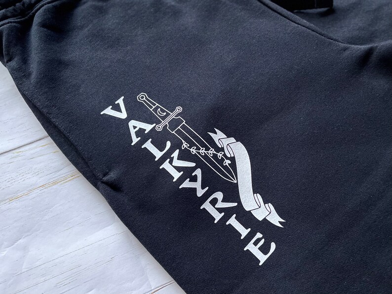 May include: Black sweatpants with a white graphic design of a sword and the word "VALKYRIE" on the left leg.