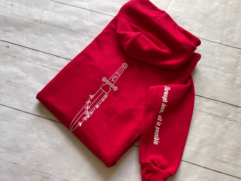 May include: Red hooded sweatshirt with a white sword design on the front and the text "Through love, all is possible" on the sleeve.