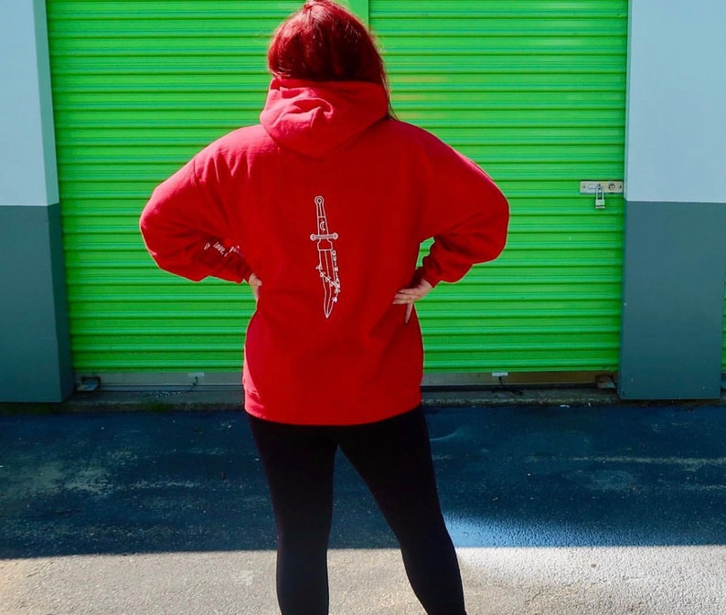 May include: Red hooded sweatshirt with a white graphic of a dagger on the back.