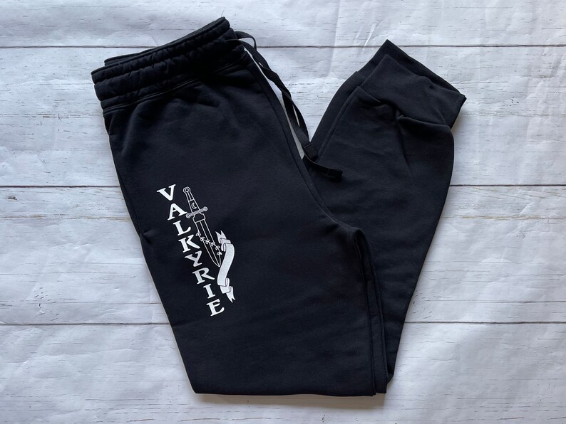 May include: Black sweatpants with a white graphic of a sword and the word "VALKYRIE" on the left leg.