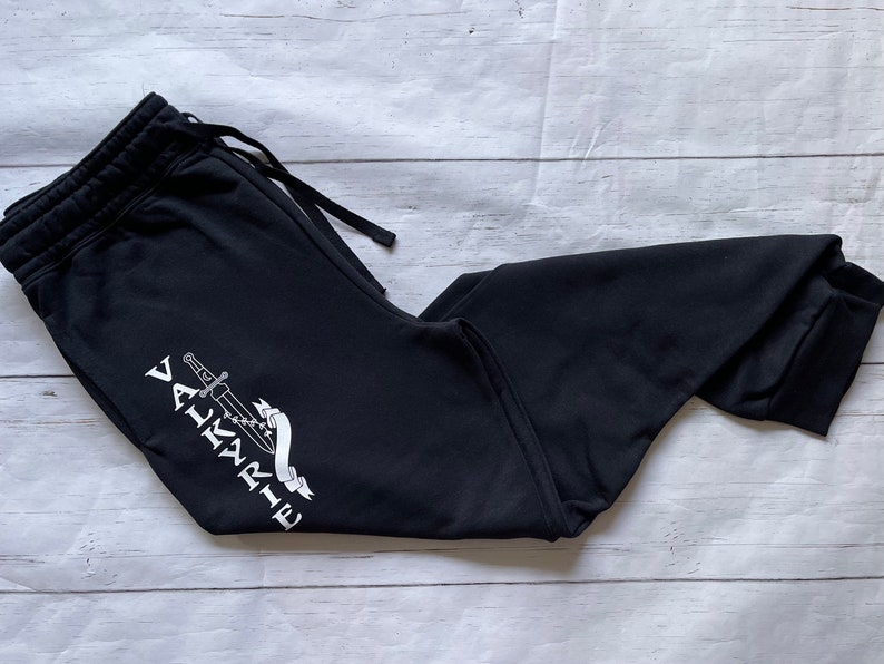 May include: Black sweatpants with a white graphic of a sword and the word "VALKYRIE" on the left leg.