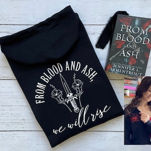 May include: Black hooded sweatshirt with a white graphic design featuring a dagger and flowers with the text "From Blood and Ash, we will rise". The book "From Blood and Ash" by Jennifer L. Armentrout is also pictured.