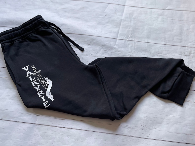 May include: Black sweatpants with a white graphic of a sword and the word "VALKYRIE" on the left leg.