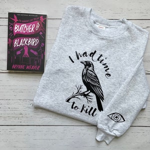 May include: A gray sweatshirt with the text "I had time to kill" and a black crow illustration. The sweatshirt also has a black eye graphic on the sleeve. A book titled "Butcher & Blackbird" is in the background.