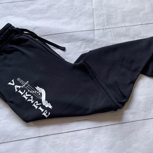 May include: Black sweatpants with a white graphic of a sword and the word "VALKYRIE" on the left leg.