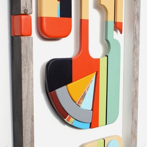 Puede incluir: Una pieza de arte de pared geom&eacute;trico abstracto enmarcado con una variedad de colores, incluyendo rojo, naranja, amarillo, verde, azul y negro. La pieza est&aacute; hecha de madera y tiene un aspecto r&uacute;stico y hecho a mano.