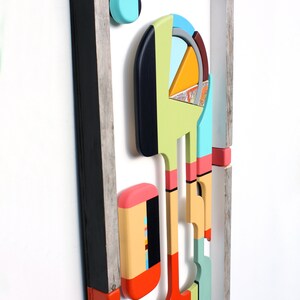 Puede incluir: Arte de pared geom&eacute;trico abstracto hecho de madera con una variedad de colores, incluyendo negro, blanco, rojo, naranja, amarillo, verde, azul y rosa. El arte est&aacute; enmarcado en un marco de madera r&uacute;stico.