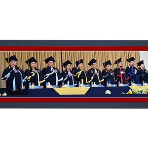 May include: A group of people in graduation attire, including black gowns, mortarboards, and stoles. The gowns have yellow and white accents. They are standing behind a table with a blue and yellow cloth, with their hands over their hearts.