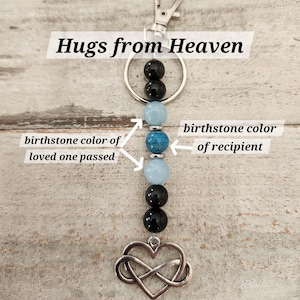 May include: A silver keychain with the words "Hugs from Heaven" and an infinity heart charm. The keychain has black and blue beads, with the blue beads representing birthstone colors.