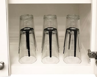 May include: Three clear glass cups with black metal stands are stacked inside a white cupboard.