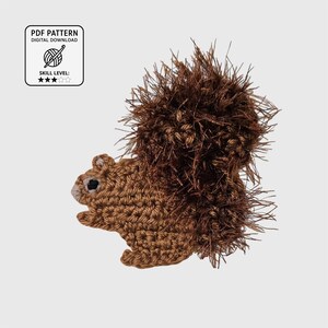 May include: A crochet squirrel applique featuring a smooth light brown body and a large, textured dark brown fuzzy tail. The design includes a small black eye and a light brown snout. The image includes a label stating PDF PATTERN DIGITAL DOWNLOAD.