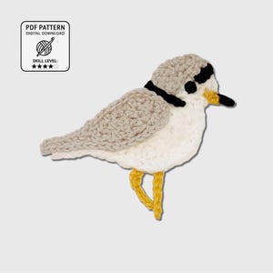 May include: A crochet applique of a bird featuring a light gray head and wing, a white chest, a black collar and eye patch, a yellow beak, and yellow legs. A square label in the top left corner reads PDF PATTERN DIGITAL DOWNLOAD SKILL LEVEL.