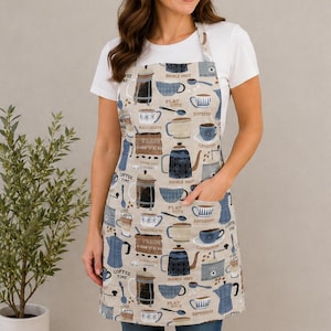 May include: A beige apron featuring a repeating pattern of various coffee-related illustrations, including coffee pots, mugs, and spoons, with text labels such as "Double Shot," "Flat White," "Espresso," "Macchiato," and "Fresh Coffee."