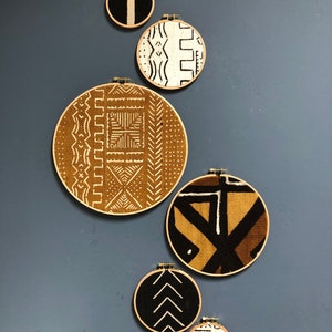 May include: Six round wall hangings with different geometric patterns in black, white, and brown. The hangings are made of fabric and are framed in wood.