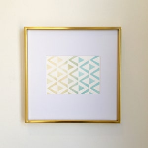 Pode incluir: Uma impressão emoldurada com um padrão geométrico de triângulos em tons de azul, verde e amarelo. A moldura é dourada.