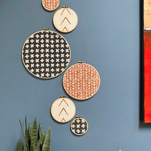 May include: A set of six round wall decor pieces with different geometric patterns. The patterns are in black, white, and brown on a beige background. The pieces are arranged in a staggered pattern on a blue wall.