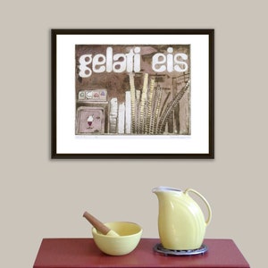 May include: A framed print of a vintage illustration of an ice cream shop with the text "gelati eis" in white letters. The print is on a white background and is framed in a black frame. The print is hanging on a light beige wall.