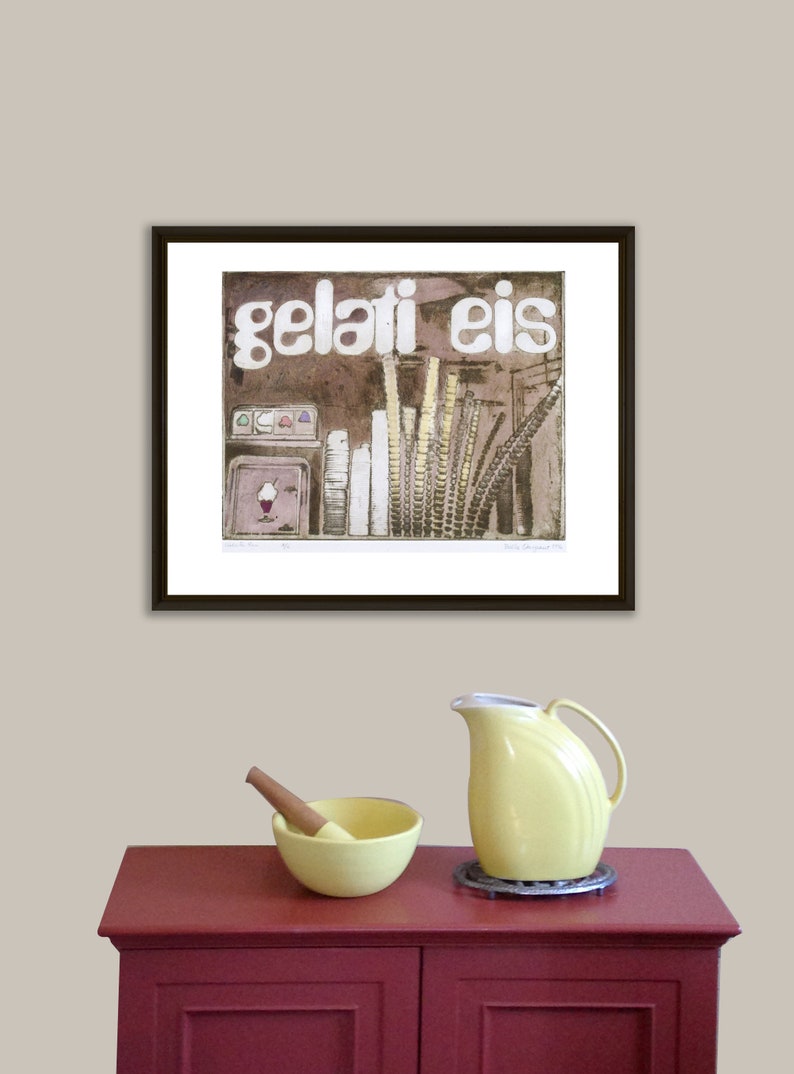 May include: A framed print of a vintage illustration of an ice cream shop with the text "gelati eis" in white letters. The print is on a white background and is framed in a black frame. The print is hanging on a light beige wall.