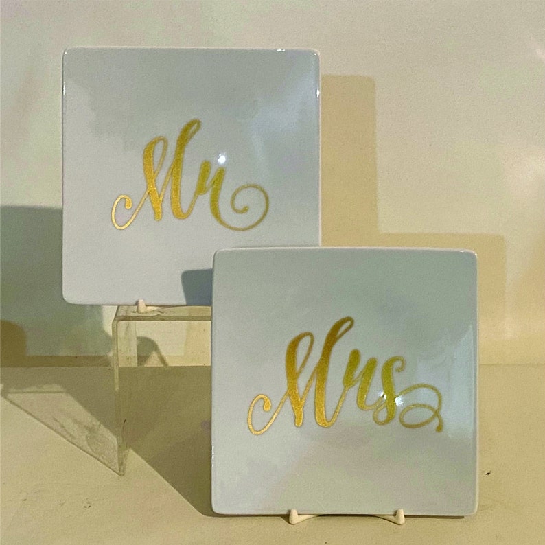 May include: Two white square ceramic plates with gold lettering. The top plate says "Mr." and the bottom plate says "Mrs."