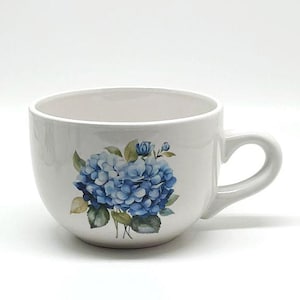 May include: A white ceramic mug with a black handle and the text "But First, Coffee" in a black, handwritten-style font. The mug is on a white surface.