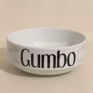 May include: White ceramic bowl with the word "Gumbo" printed in black on the side. The bowl is empty.