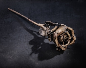 May include: A single golden rose crafted from metal, with a long stem and leaves, is displayed against a dark background.