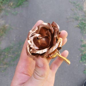 May include: A copper rose sculpture with a detailed, realistic design. The rose is crafted from metal and has a textured, hammered finish.