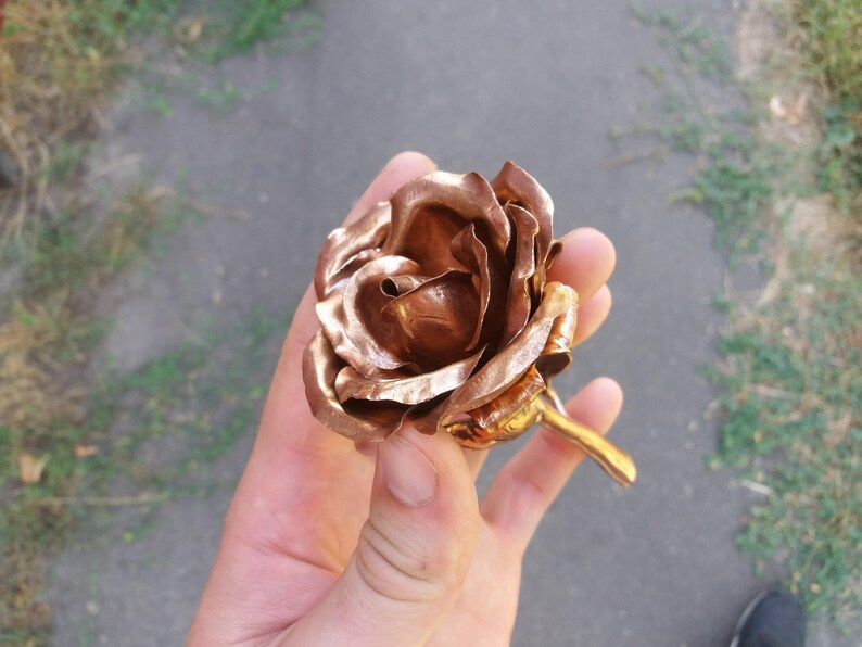 May include: A copper rose sculpture with a detailed, realistic design. The rose is crafted from metal and has a textured, hammered finish.