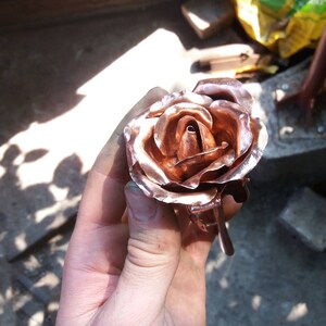 May include: A copper rose sculpture with a detailed, realistic design. The rose is crafted with intricate petals and a delicate stem.